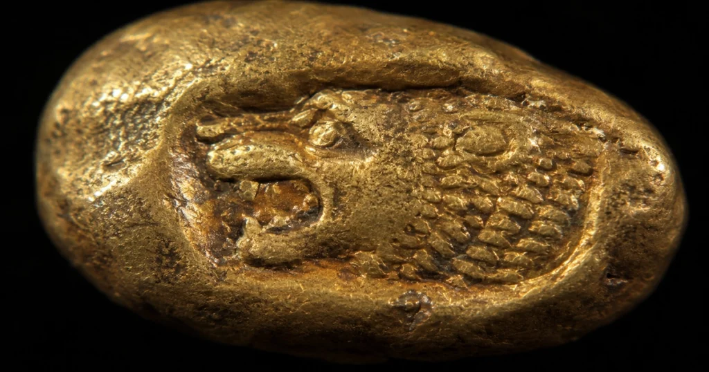 An extreme close-up of a lydian electrum coin showing the crude, irregular shape stamped with the iconic roaring lion motif, representing the dawn of standardized coinage in the history of gold.